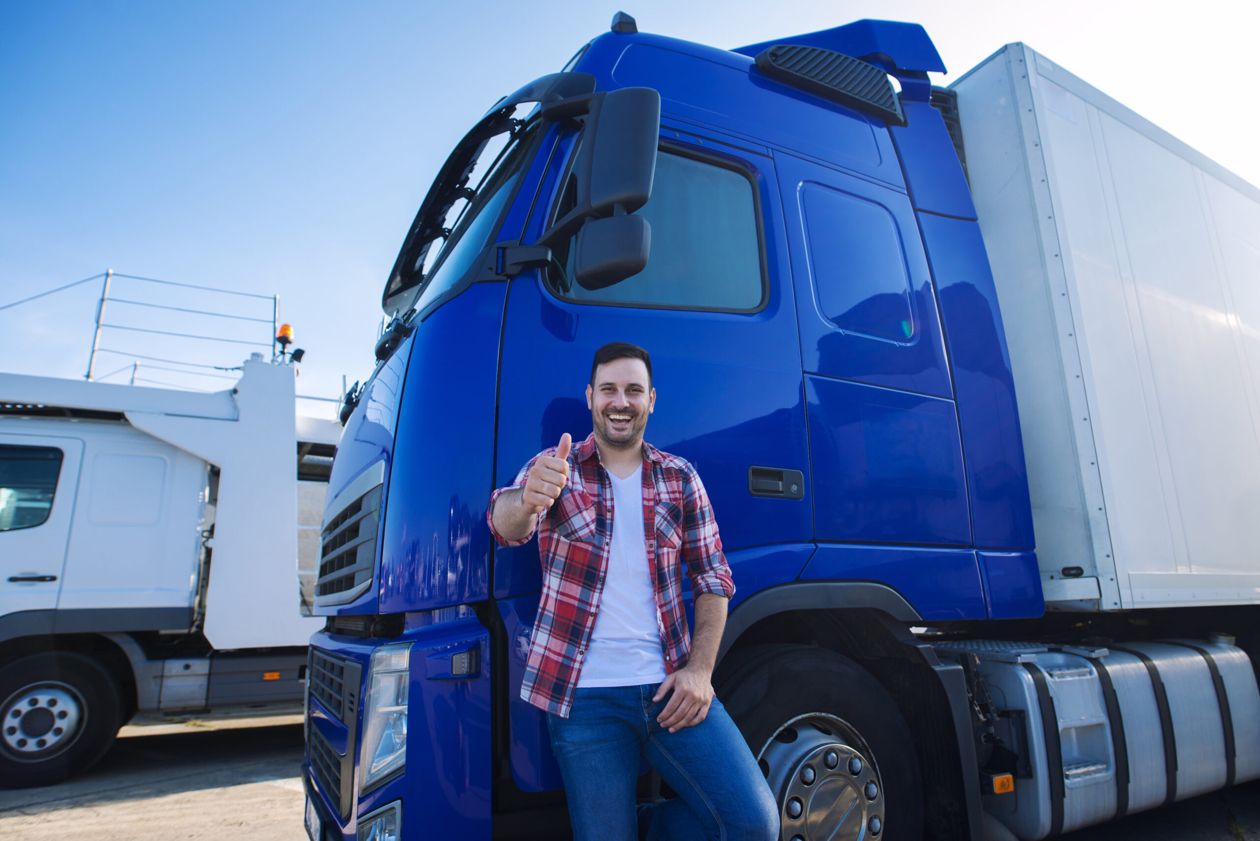 Professional truck driver in front of long transportation vehicle holding thumbs up ready for a new ride.